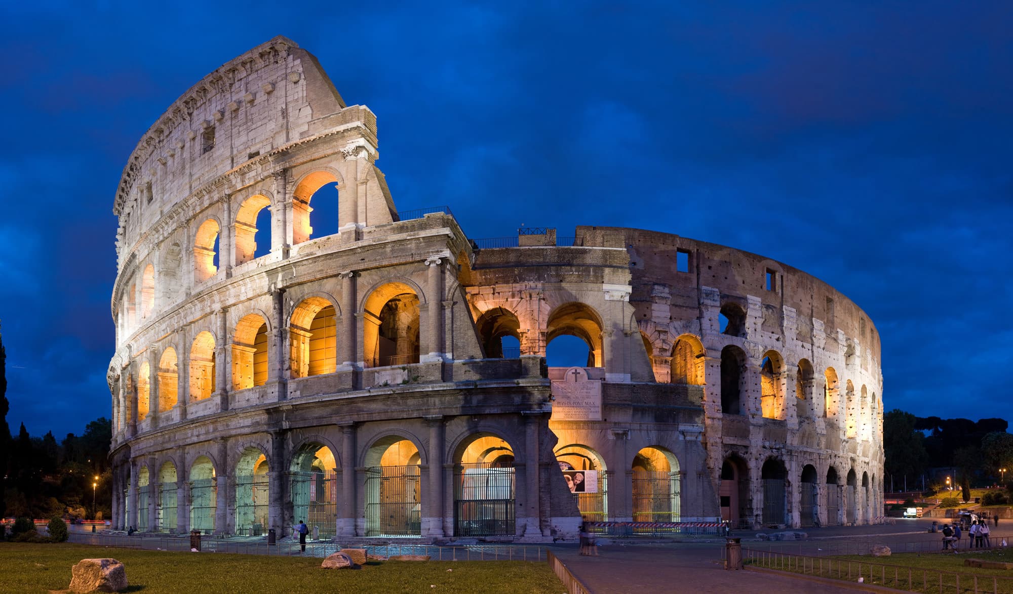 Colosseum di Rom diterangi pada waktu senja, dengan gerbang dan dinding luar kelihatan.