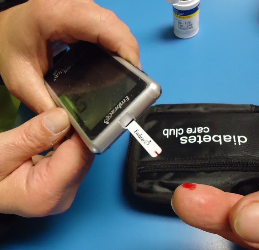 A person using a small glucose meter after taking a fingertip blood sample.