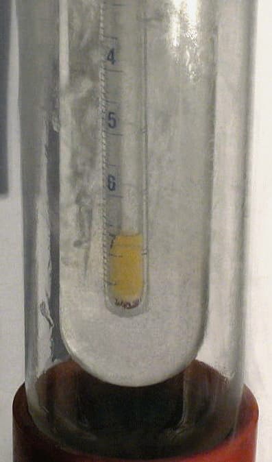 A tube containing pale yellow liquid fluorine in a cryogenic bath.