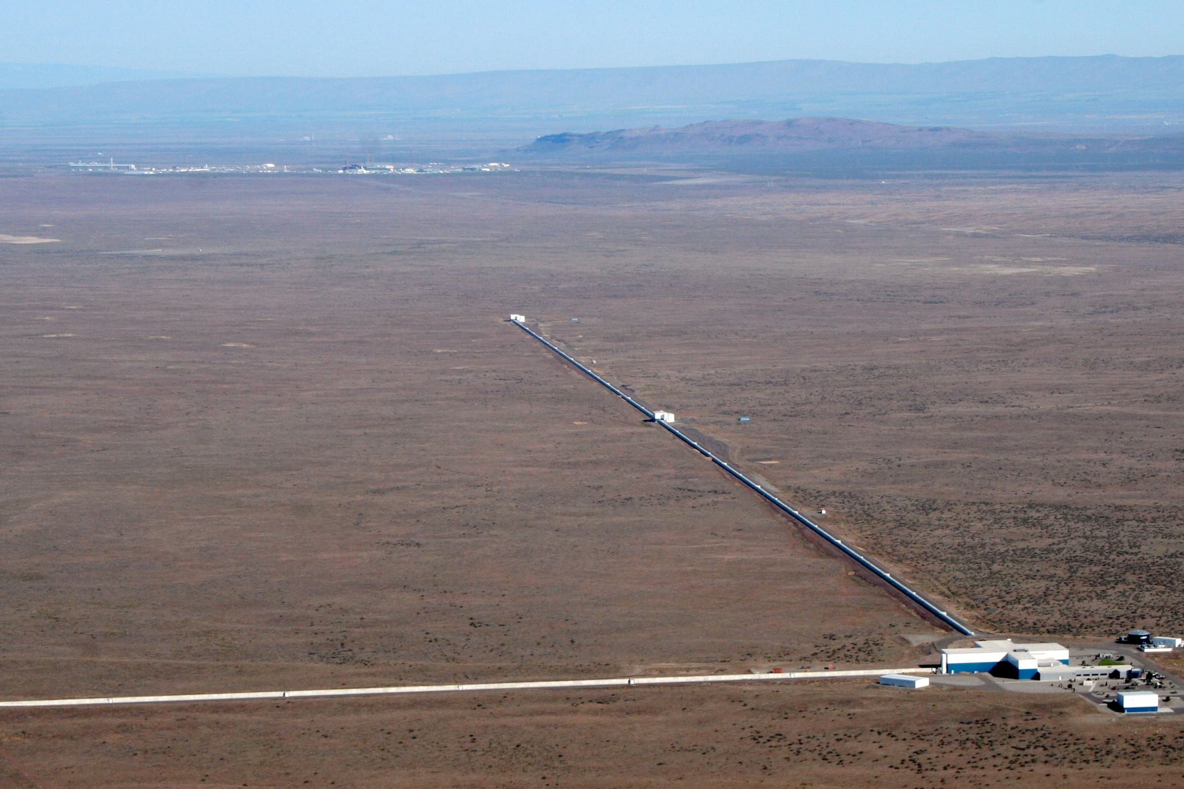 Aerial view of the LIGO Hanford Observatory with two long perpendicular arms crossing desert terrain.