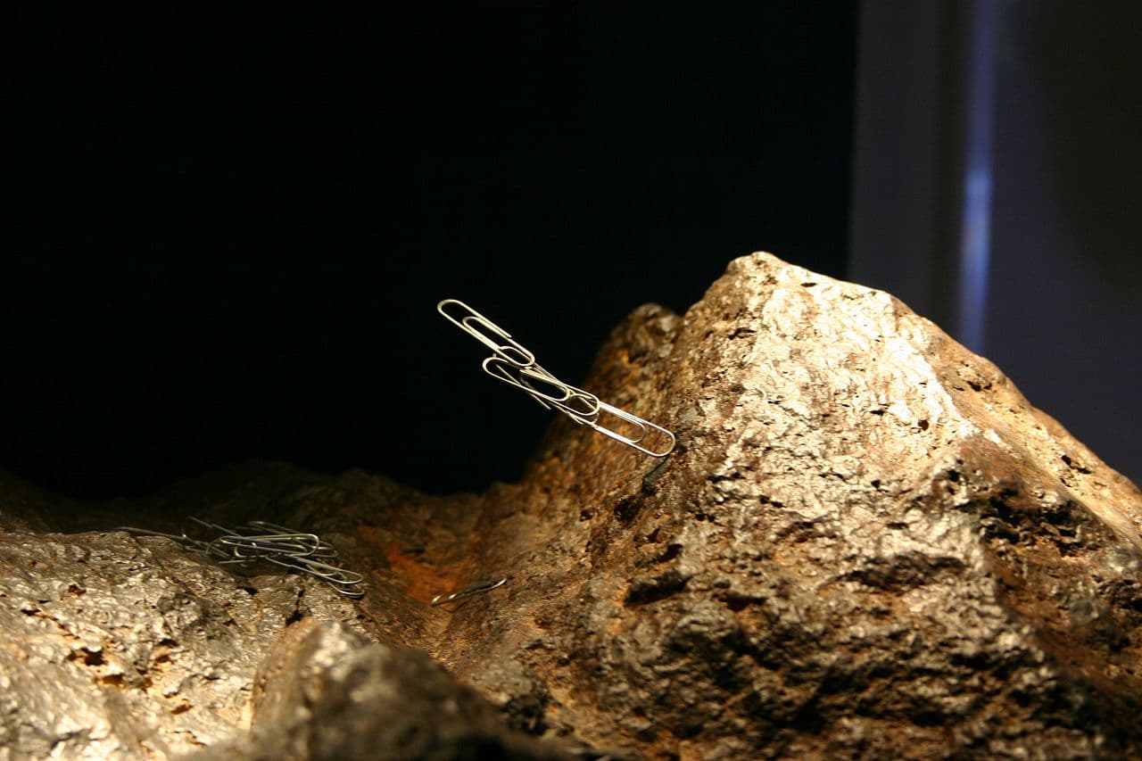 A lodestone attracting small metal paper clips on a white surface.