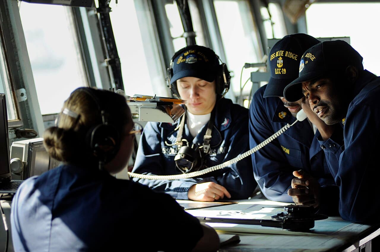 A sailor checks a navigational chart in the pilot house of a ship.