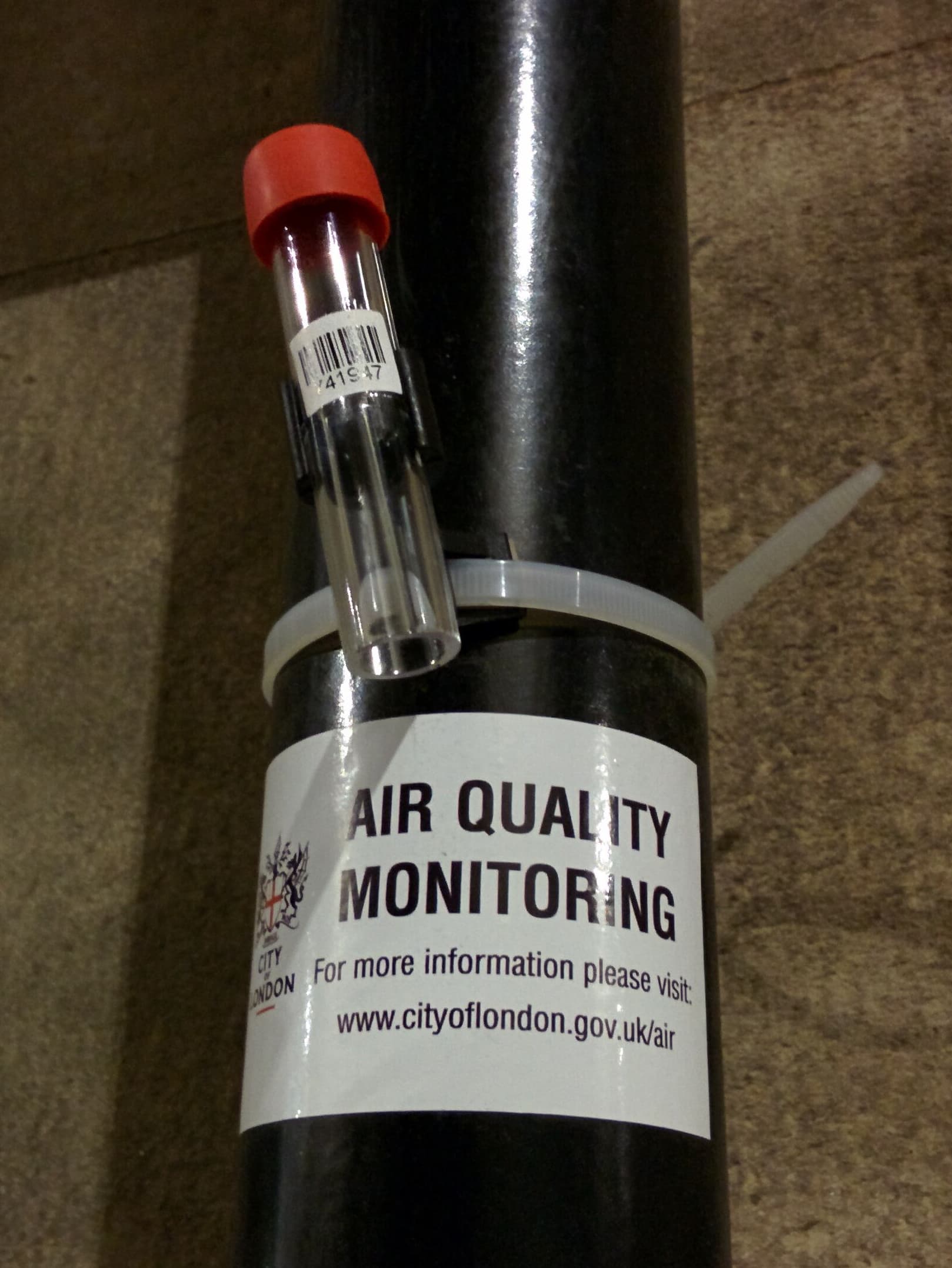 A nitrogen dioxide diffusion tube installed on a street sign for air quality monitoring in London.